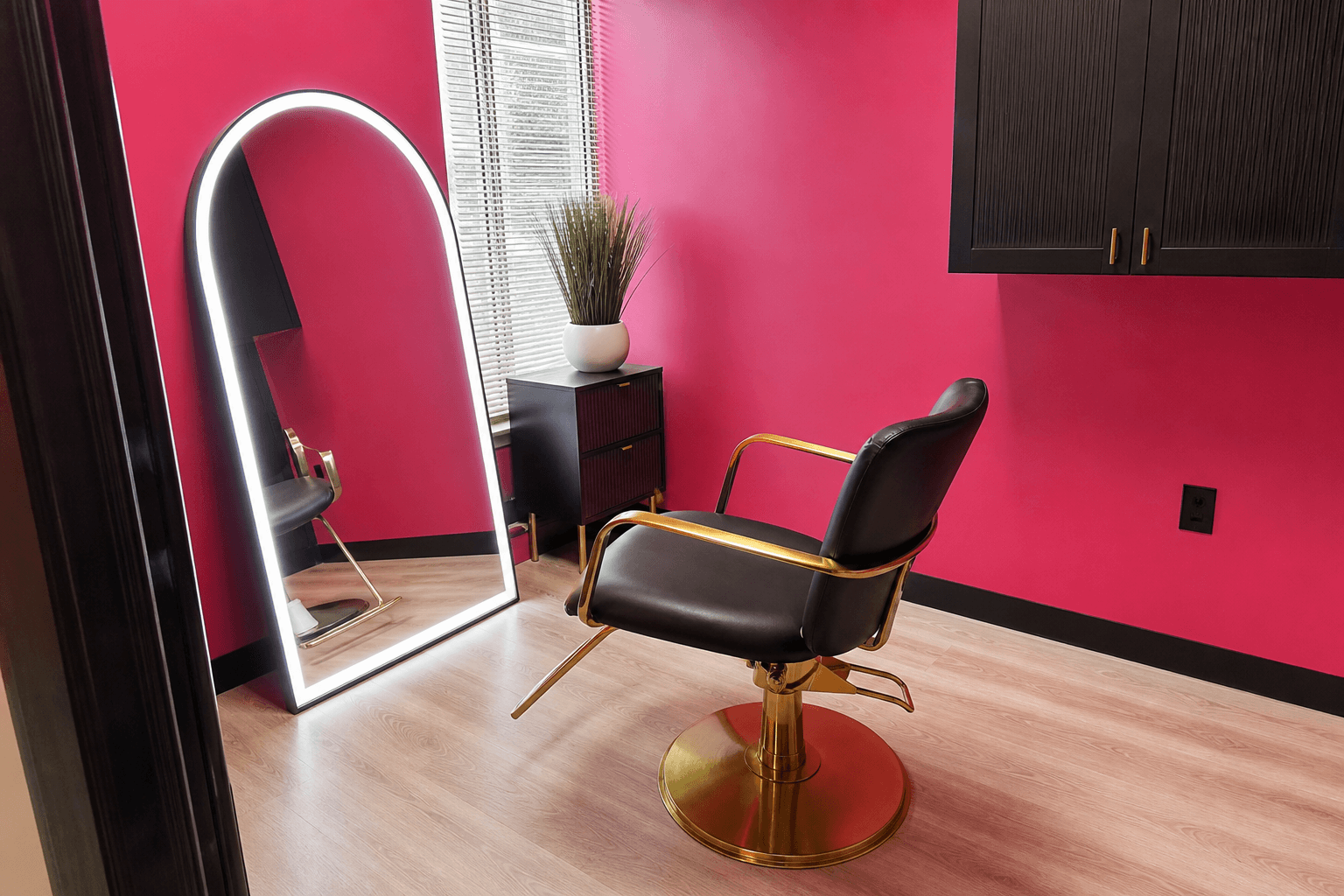 Salon suite with pink walls, gold styling chair and arched LED mirror